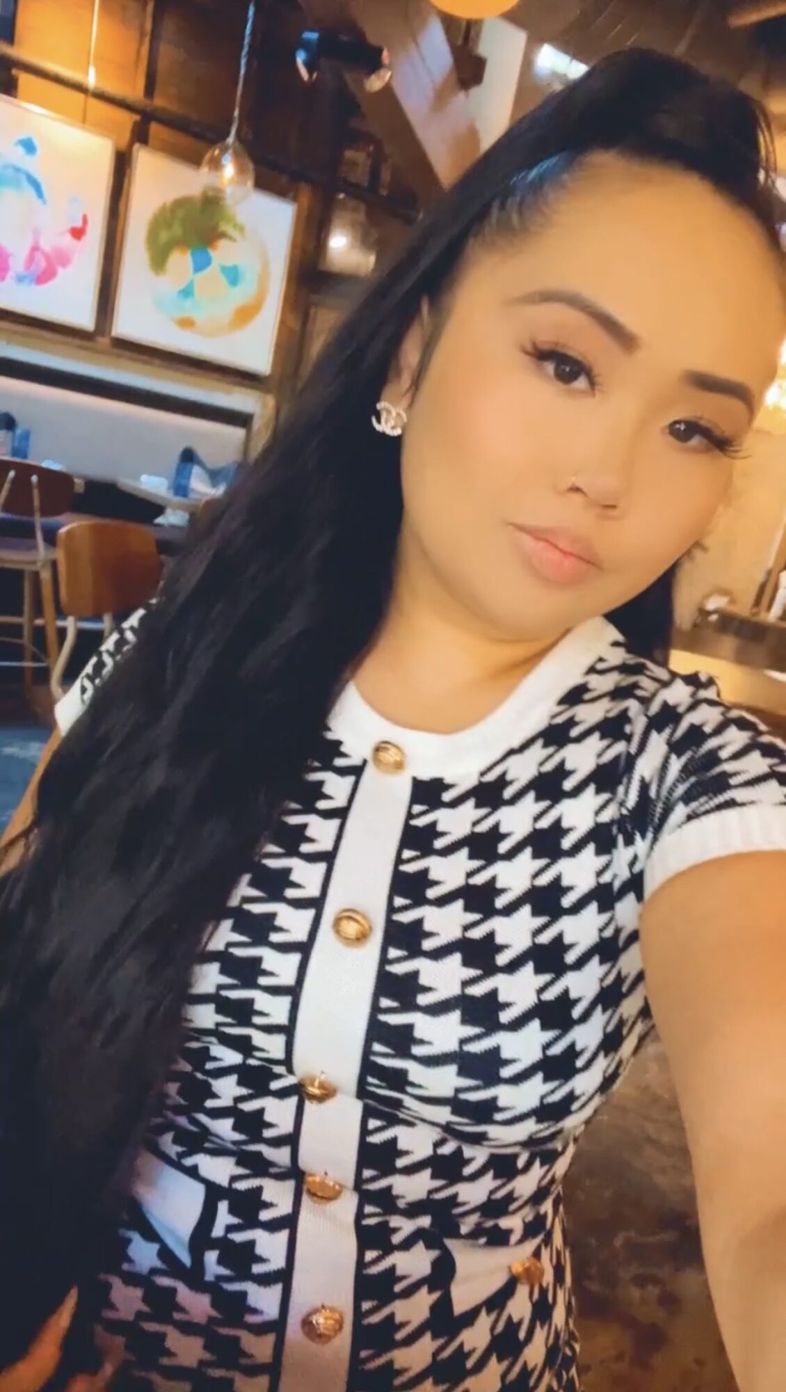 Woman with long dark hair taking a selfie in a restaurant or cafe setting.