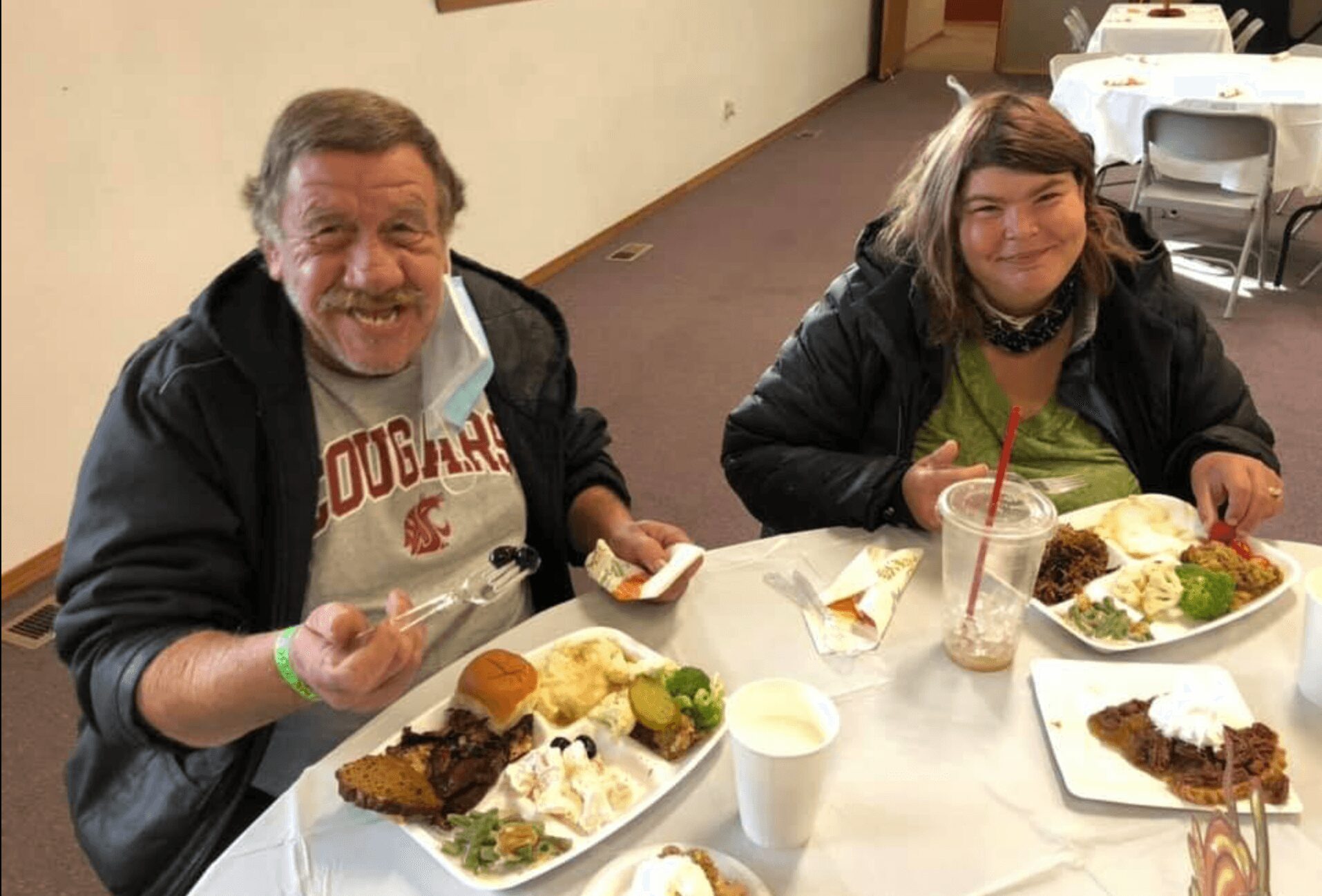 Two people sitting at a table with plates of food, smiling, in a dining area.